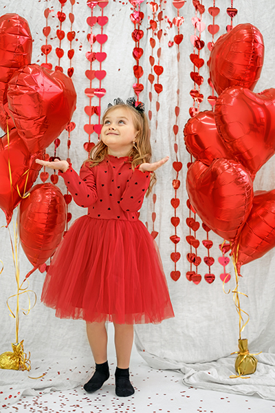 A girl in a red dress surrounded by air foil balloons catches falling confetti. Celebrating Valentine's Day