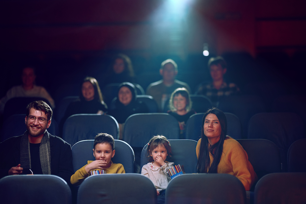 A modern family enjoys quality time together at the cinema, indulging in popcorn while watching a movie with their children.